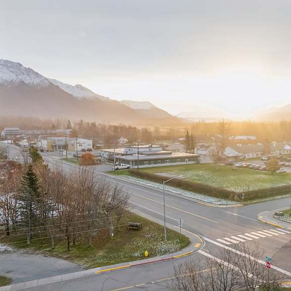 a street view of a residential area with houses, trees, and mountains in the background.