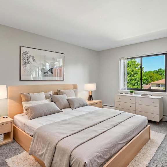 a bedroom with a large bed, two lamps, a dresser, and a potted plant.