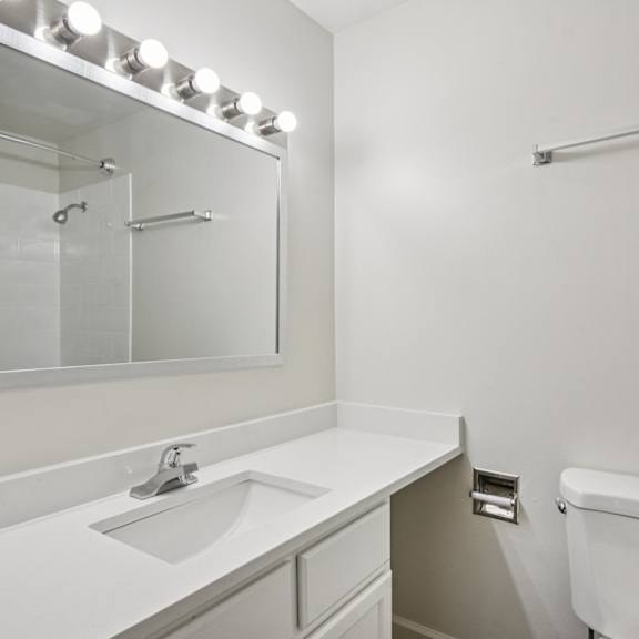 a white bathroom with a sink, toilet, and mirror.