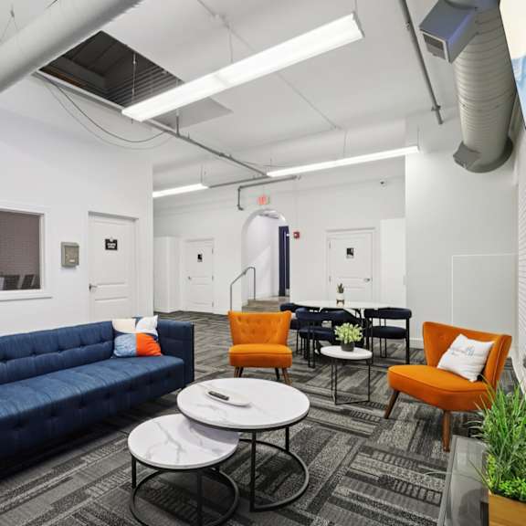 a blue couch is in the middle of a room with orange chairs and a white table.