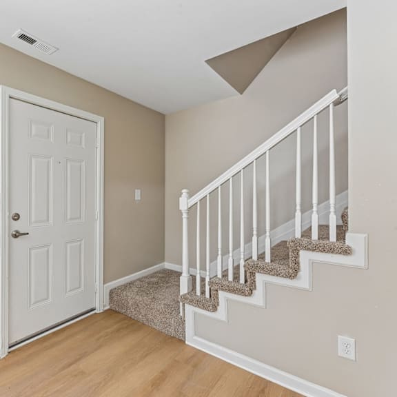 a white door is on the left and a staircase with a beige carpet is on the right.