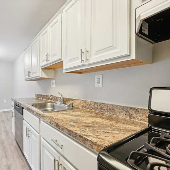an empty kitchen with white cabinets and granite counter tops and a stove and microwave at renew odenton