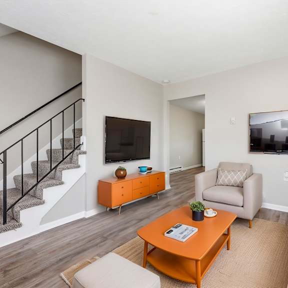 a living room with a staircase, a couch, a chair, a coffee table, and a television.