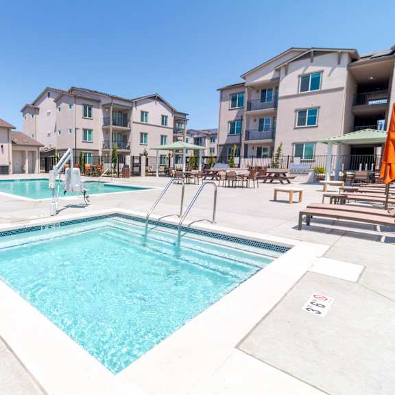 a hot tub with a swimming pool and apartment buildings in the back