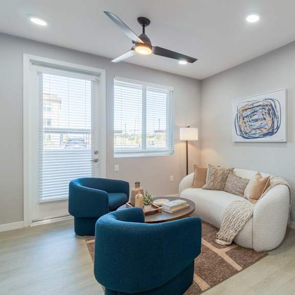 a living room with a blue chair, a white couch, and a ceiling fan.