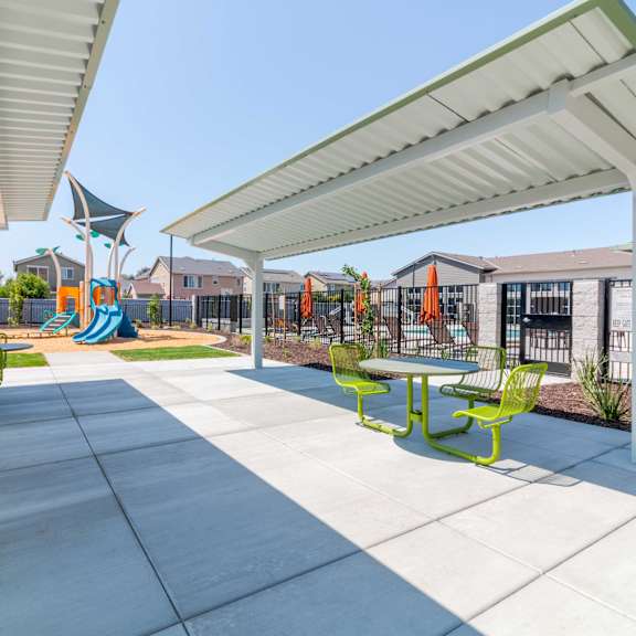 a courtyard sitting area with shade and a playground in the background