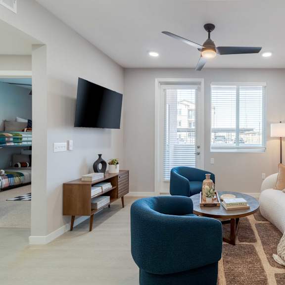 a living room with a blue armchair, a white sofa, and a ceiling fan.