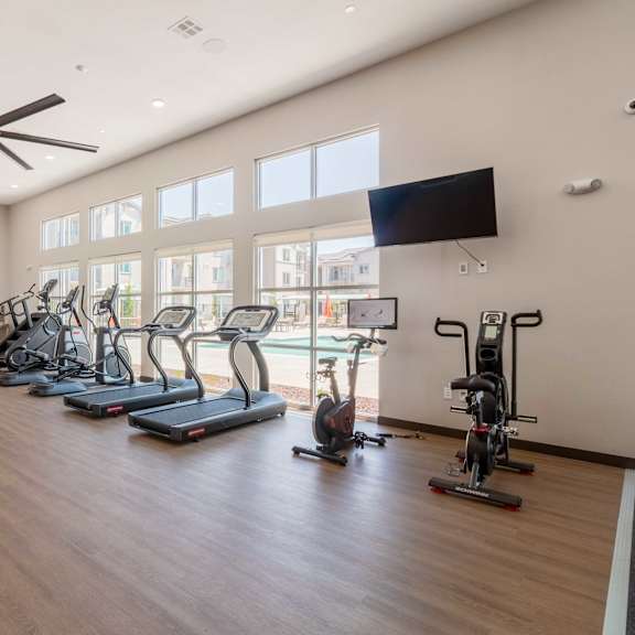 a spacious gym with a variety of exercise equipment and a ceiling fan.