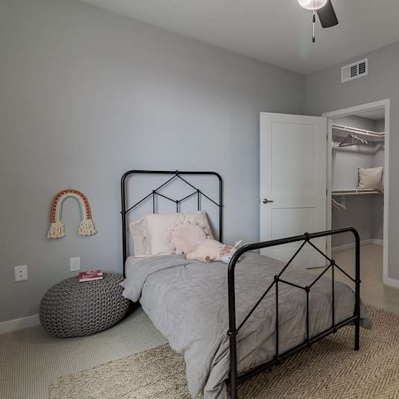 a bedroom with a bed, a rug, a ceiling fan, and a door leading to another room.