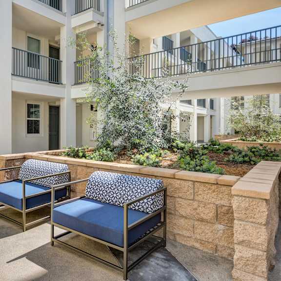 a seating area with two blue chairs and a stone wall in front of a building