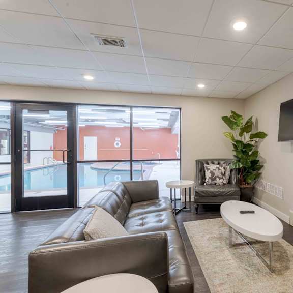 a living room with a brown leather couch, a white coffee table, and a flat screen tv mounted on the wall.
