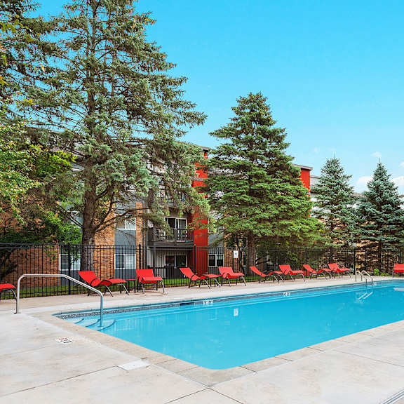 a swimming pool with red chairs around it in front of a building