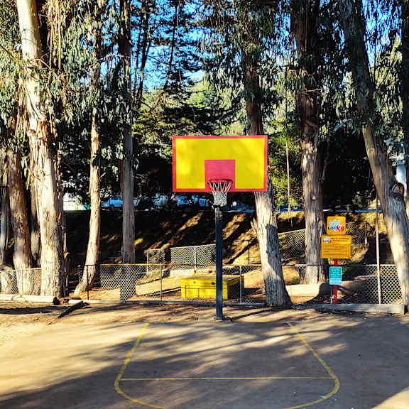 a basketball court surrounded by trees with a yellow hoop at salinas sunset apartments, salinas