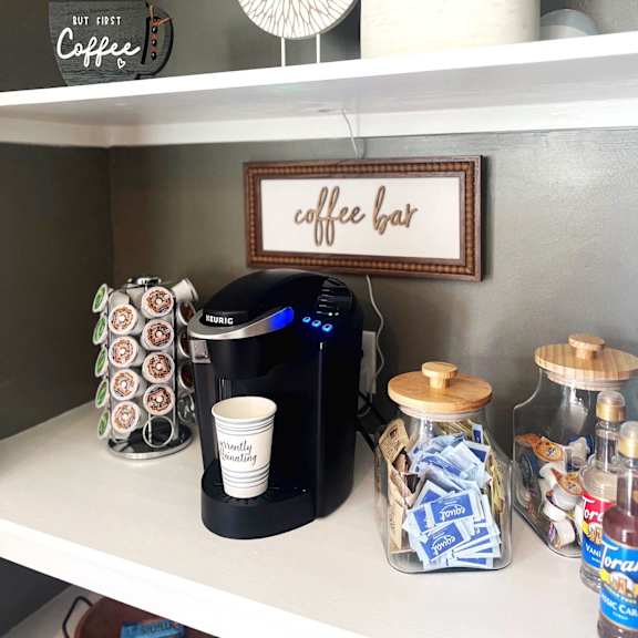 a coffee bar in a kitchen with a coffee maker and coffee cups on a shelf