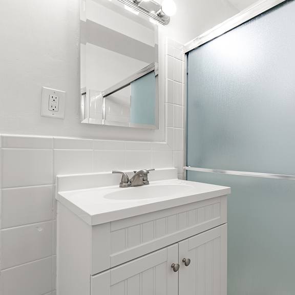 a white bathroom with a sink, mirror, and shower at the exeter apartments, apartments, seattle, wa