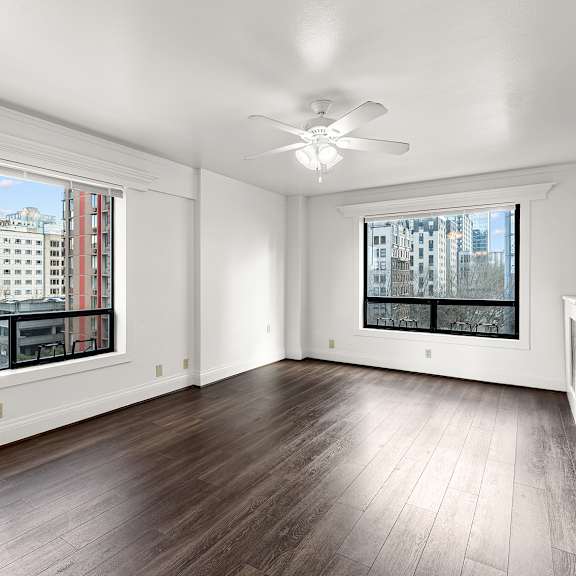 a room with a ceiling fan and two windows overlooking a cityscape at the exeter apartments, washington