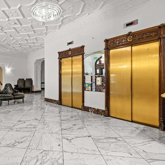 a white marble hallway with a black and gold elevator at the exeter apartments, seattle