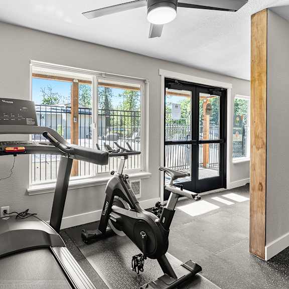 a treadmill and a stationary bike are in a room with a ceiling fan.