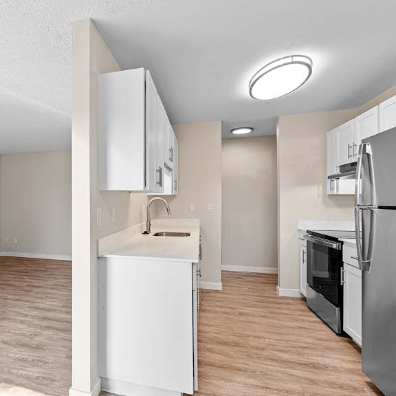 a kitchen with white cabinets and a refrigerator with a view of the living room