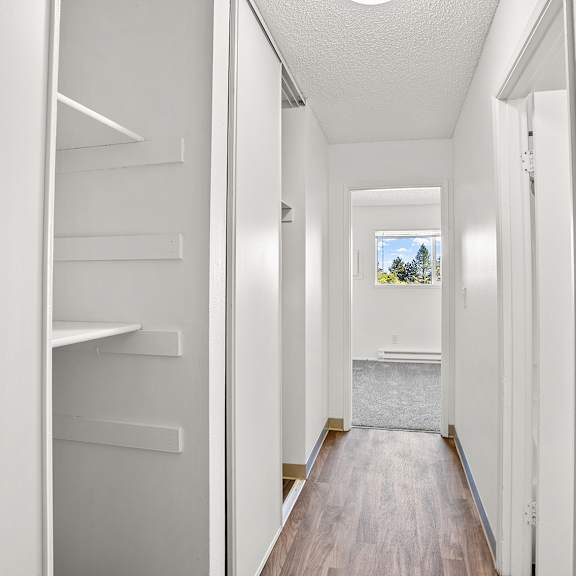 a long hallway with white walls, wood floors, and storage