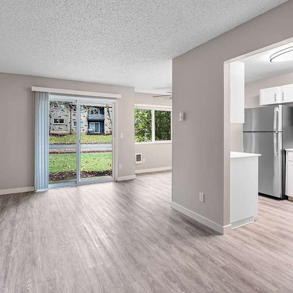 a spacious room with a view of a green lawn and a building through the sliding glass door.