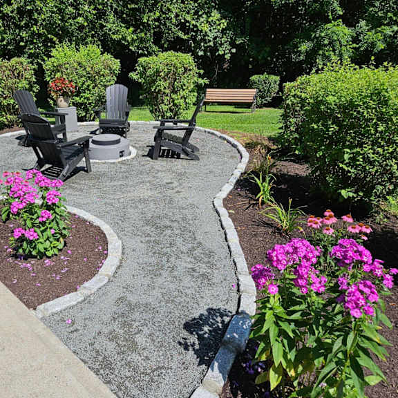 a garden with a circular concrete table surrounded by chairs and flowers.