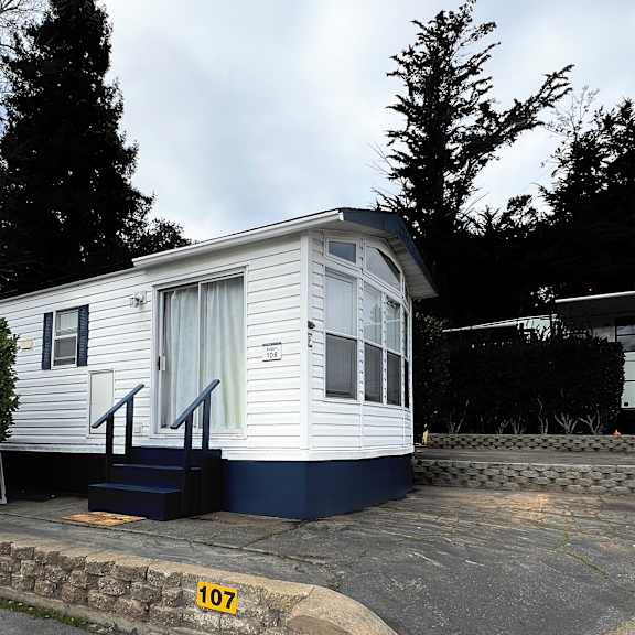 a small white house with a blue staircase and a number 107 on the ground.