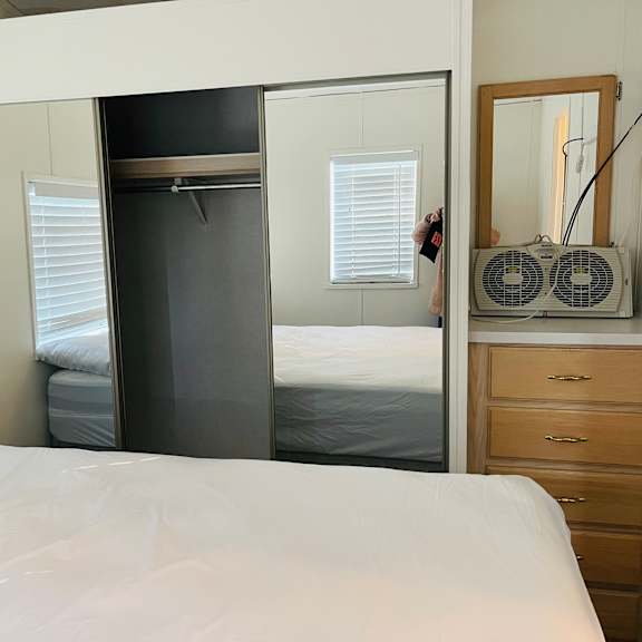 a bedroom with a white bed, a wooden dresser, and a mirror.