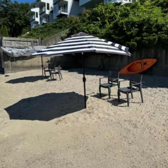 a striped umbrella is open over a table and chairs on a sandy beach along the lake at little eagle bay apartments, vermont, 05408