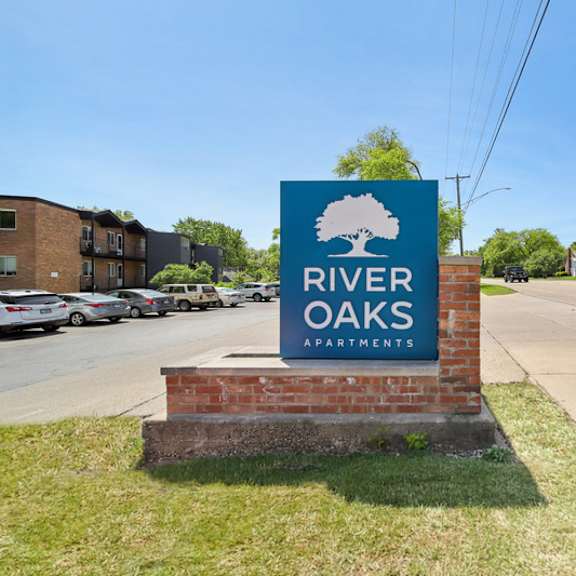 a sign for river oaks apartments is displayed in front of a parking lot.