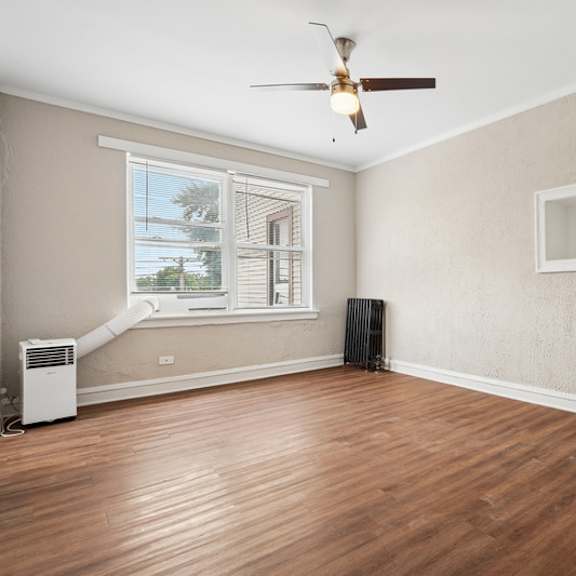 a room with a ceiling fan, a window with blinds, a radiator, a door, and a wooden floor.