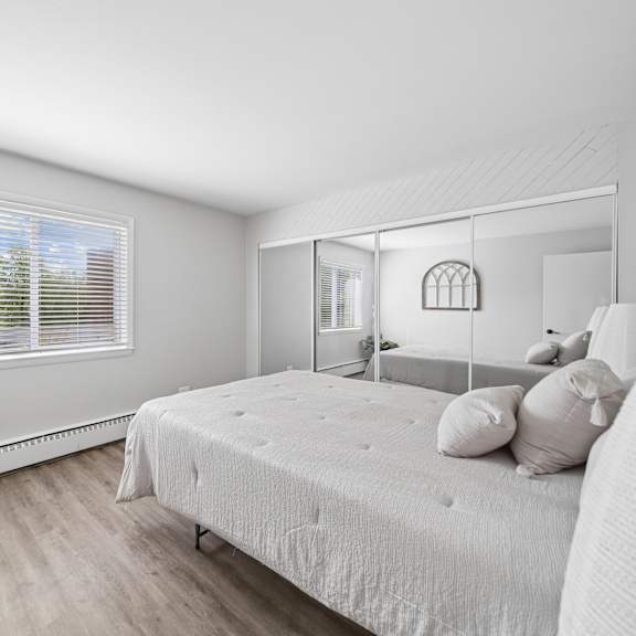 a bedroom with a bed, a potted plant, and a window with blinds.