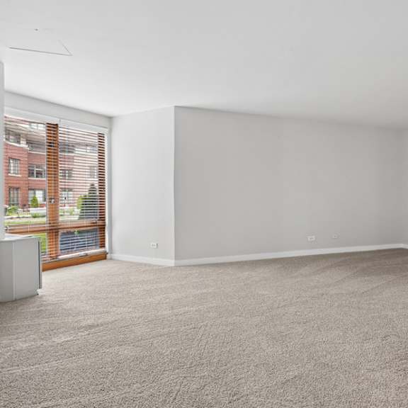 a large empty room with a carpeted floor and a window with blinds.