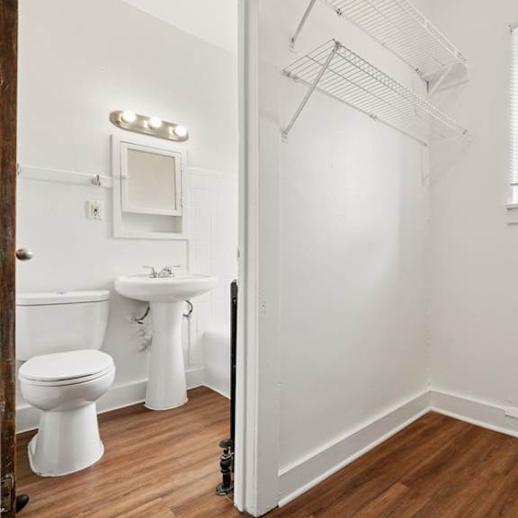 a white bathroom with wood flooring and a window.