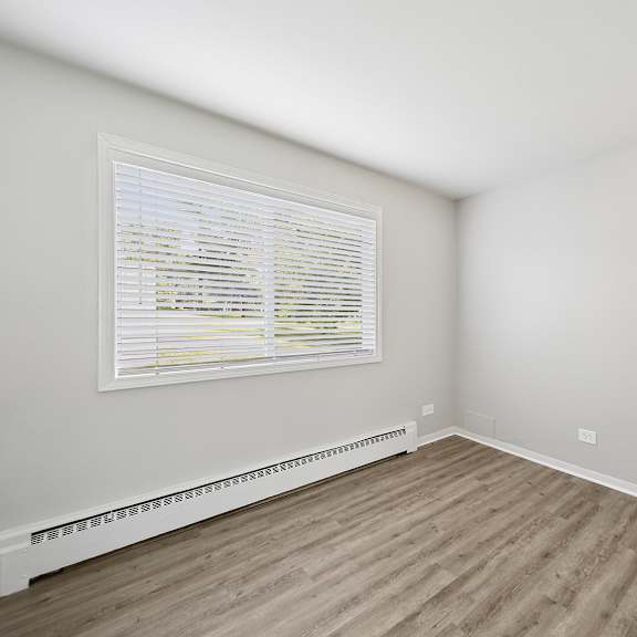 a room with a white door, window with blinds, and a radiator on the wall.