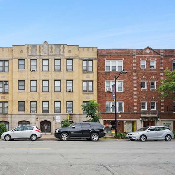 a row of three-story buildings with cars parked in front.