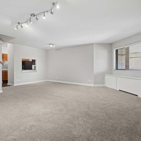 a spacious room with a carpeted floor and a staircase on the left side.