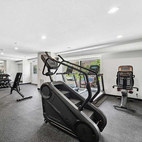 a black treadmill is in the foreground of a well-equipped gym.