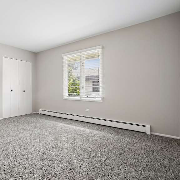 a room with grey carpet, white cupboards and a window.