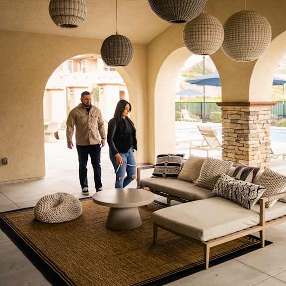 a couple walks through a living room with couches and lamps