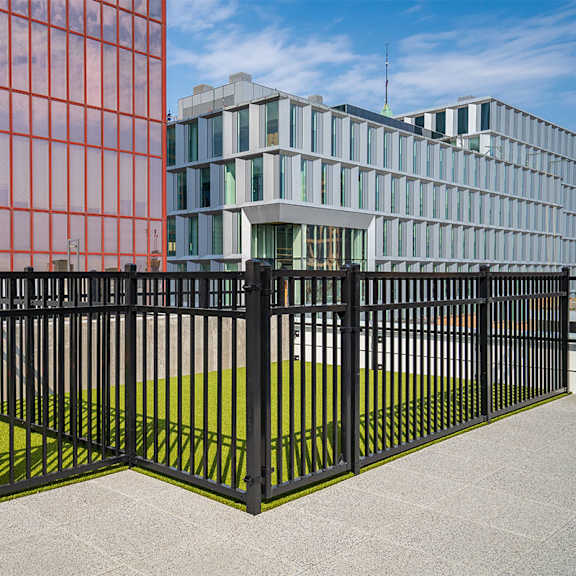 a black metal fence with a green lawn in front of a red building. at sora apartments, minneapolis, mn, 55415