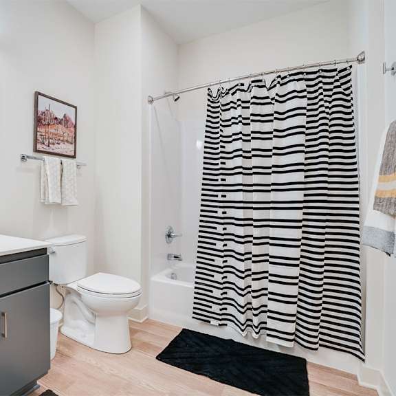 a bathroom with a white toilet, sink, and a shower curtain with black stripes. at sora apartments, minneapolis, minnesota