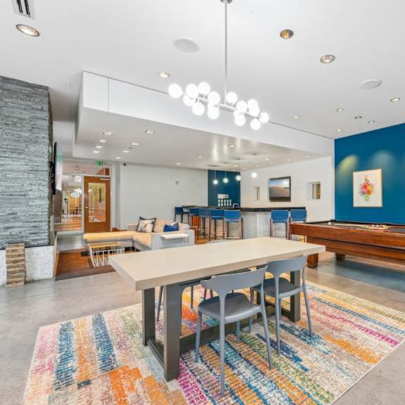 a room with a long table and chairs, a stone fireplace, and a colorful rug.