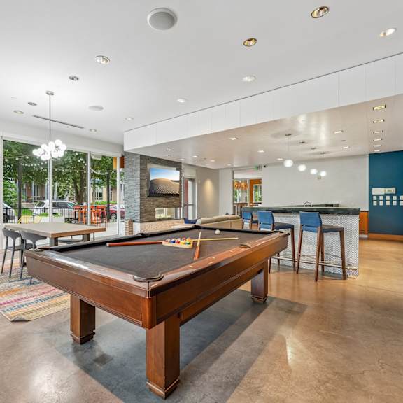 a pool table is in the middle of a room with a bar and a television.