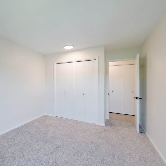 a room with white walls and carpeted floor with two white doors.