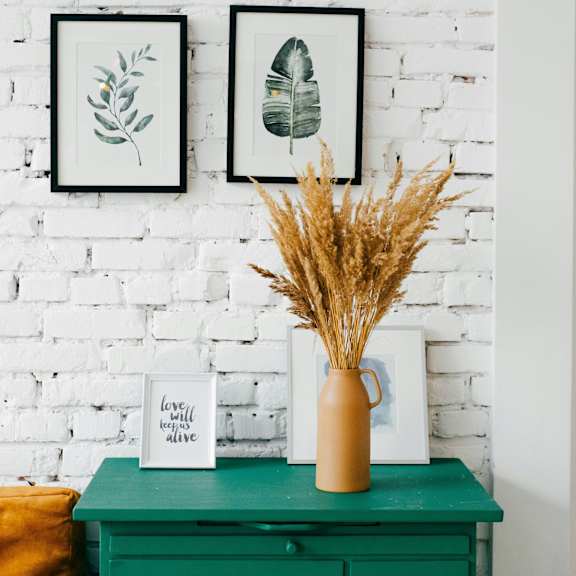 a green dresser with a vase of dried plants on top.