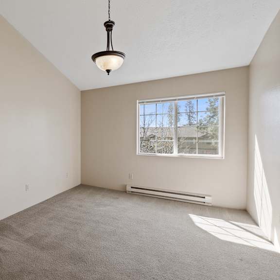 empty room with carpet, white walls, chandelier in center, and window.