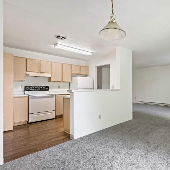 an empty living room and kitchen with white walls and wood flooring