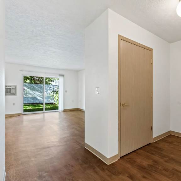 an empty living room with white walls and wooden floors and a door to a bedroom