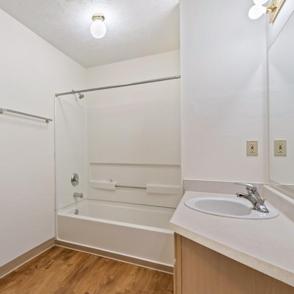 a white bathroom with a sink, mirror, and bathtub.